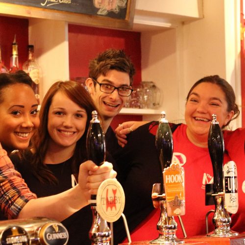 Several smiling people stand behind the bar in red T-shirts
