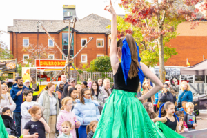 Person performing on stage at a festival wearing a blue ribbon in their hair and green skirt