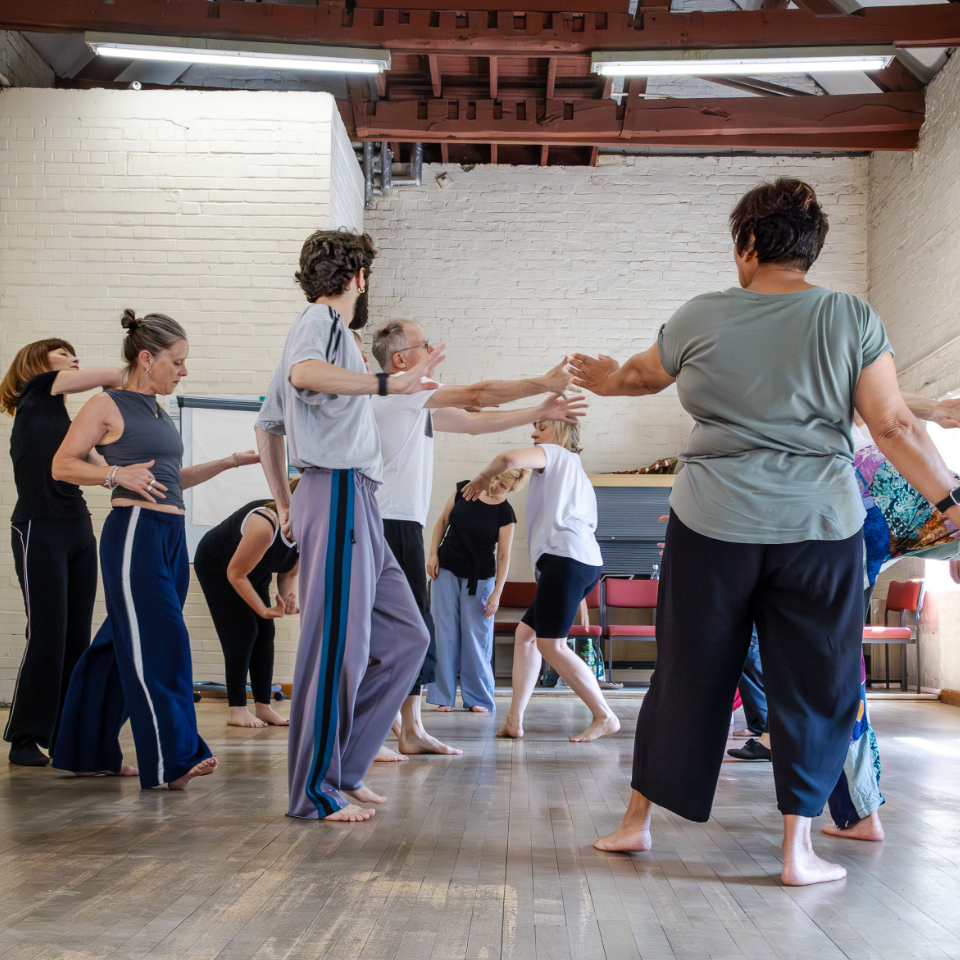 Group of people stood to the side in a dance studio with their arms stretched out